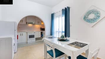 A compact kitchen with white cabinets, a white refrigerator, and a dining table with blue chairs.