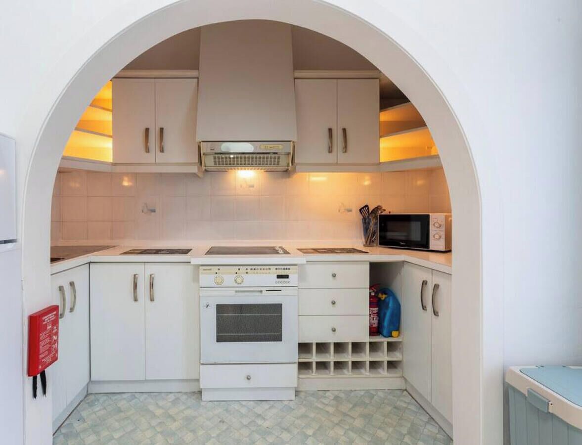 A compact kitchen with white cabinets, a built-in oven, a microwave, and a small sink.