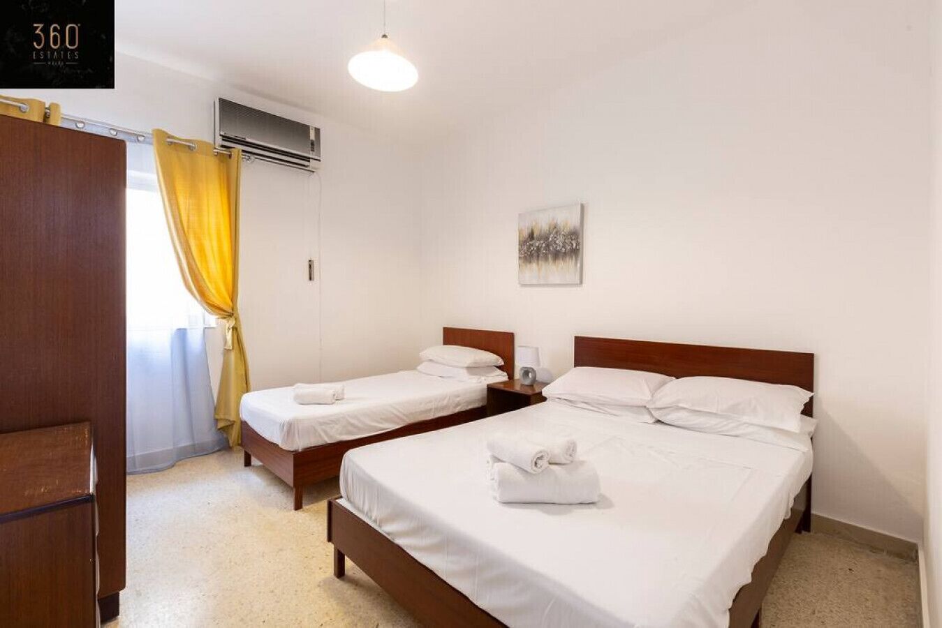 A hotel room with two single beds, a wooden wardrobe, a ceiling fan, and a painting on the wall.