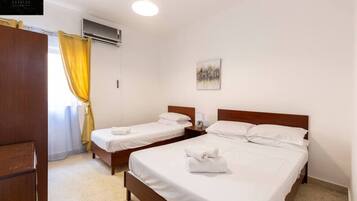 A hotel room with two single beds, a wooden wardrobe, a ceiling fan, and a painting on the wall.