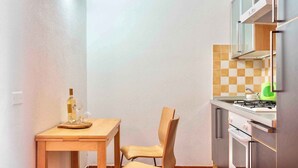A small kitchen with a wooden table and chair, a gas stove, and a microwave. - Studio for 3 people with air conditioning (Santa Teresa di Gallura)