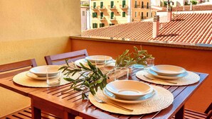 A wooden table set with plates, glasses, and olive branches on a balcony with a view of buildings. - Studio for 3 people with air conditioning (Santa Teresa di Gallura)