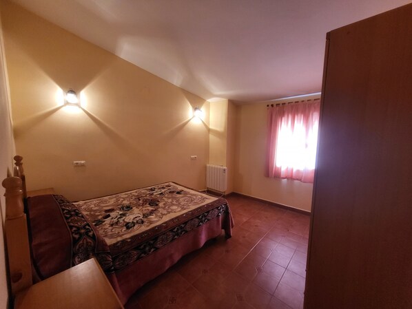 A bedroom with a bed, a nightstand, a radiator, and a window with curtains.