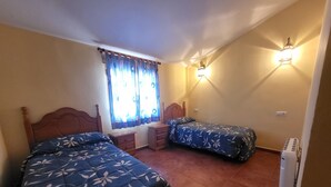 Una camera da letto con due letti, una finestra con tende, un comodino, una lampada a parete e un termosifone.