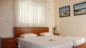 A double bed with white linens, a wooden headboard, a bedside table with a vase, and two framed pictures on the wall. - On the beach house latsi (Poli Crysochous)