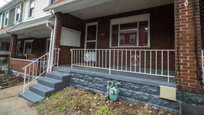 A two-story brick house with a front porch, a set of stairs leading to the entrance, and a mailbox. - Momma Mary's Place @ Lawrenceville (Pittsburgh)