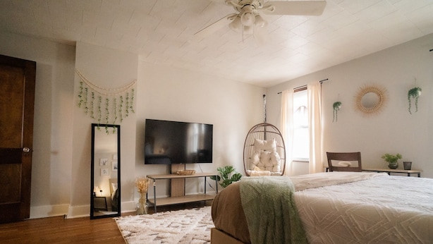 A bedroom with a bed, a television, a hanging chair, and a mirror. - Momma Mary's Place @ Lawrenceville (Pittsburgh)