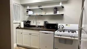 A kitchen with white cabinets, a stove, a microwave, and a sink. - Momma Mary's Place @ Lawrenceville (Pittsburgh)