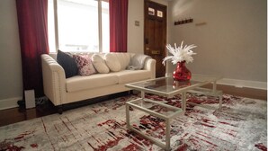 A living room with a white sofa, red curtains, a glass coffee table, and a red vase with white flowers. - Momma Mary's Place @ Lawrenceville (Pittsburgh)