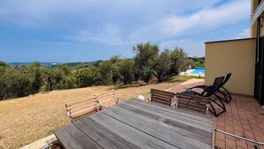 A patio with a wooden table and chairs, overlooking a pool and a hilly landscape. - Villa seaview and private pool (Torrevecchia Teatina)