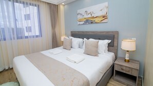 A neatly made bed with a beige and white bedspread, two pillows, and two bedside lamps. - Amani Suite by Homes By Della (Nairobi)