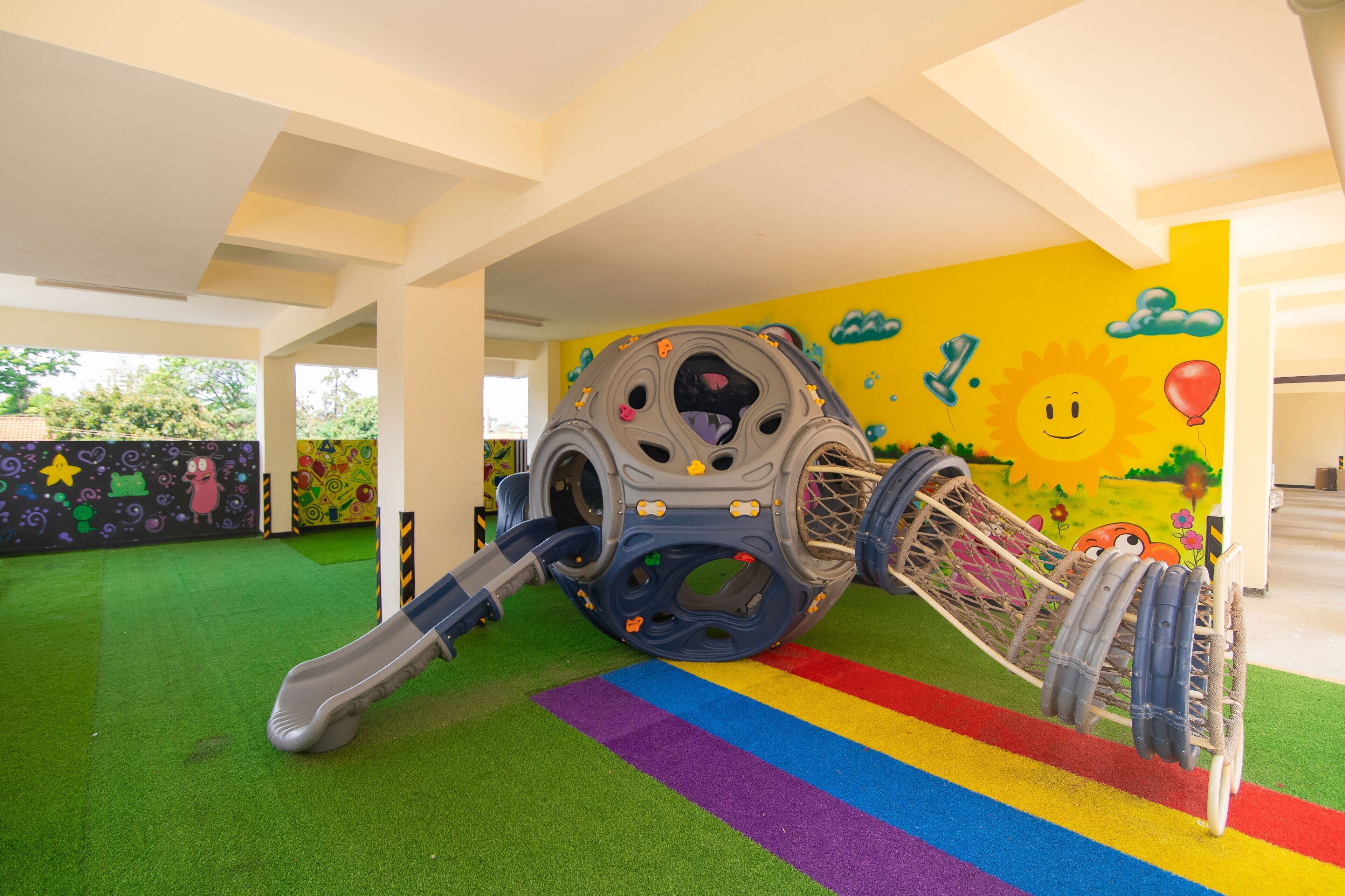 A play area with a slide, a climbing structure, and a colorful mural.