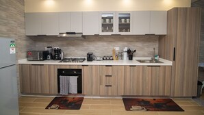 A modern kitchen with light wood cabinetry, a built-in microwave, a coffee maker, and a sink. - Amani Suite by Homes By Della (Nairobi)
