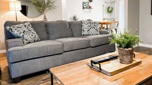 Un salon moderne avec un canapé d’angle gris, une table basse en bois et une plante en pot.