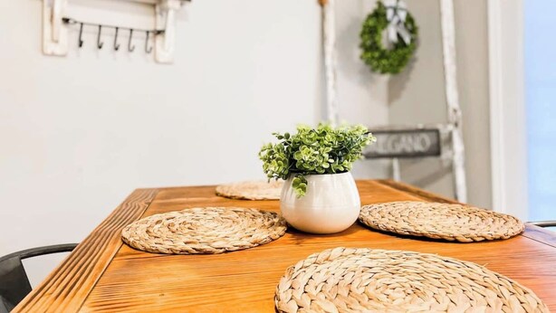 Une table à manger agrémentée de sets de table en fibres tressées, d’une plante en pot et d’un panneau d’ardoise.
