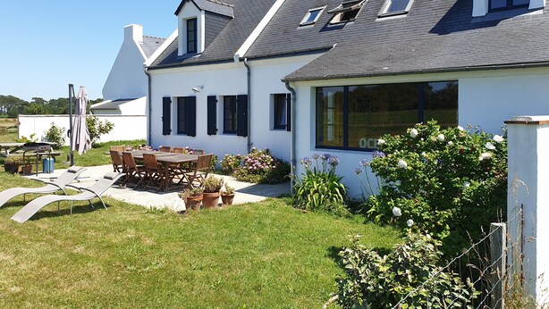 Ein zweigeschossiges Haus mit großem Vorgarten, einer Essgegend mit Gartenmöbeln und verschiedenen Blumentöpfen.