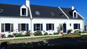 Ein weißes Gebäude mit blauen Fensterläden, einem geneigten Dach und einem Garten mit Blumen.
