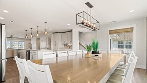 A spacious kitchen with white cabinetry, a wooden dining table, and pendant lighting. - Lotus House Pets Stay Free +Private Pool (Kill Devil Hills)