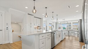 A modern kitchen with white cabinetry, stainless steel appliances, and pendant lighting. - Lotus House Pets Stay Free +Private Pool (Kill Devil Hills)