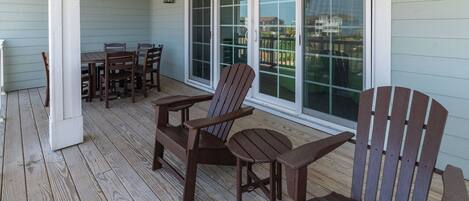 A covered porch with wooden chairs and a table, large windows, and a view of a residential area.