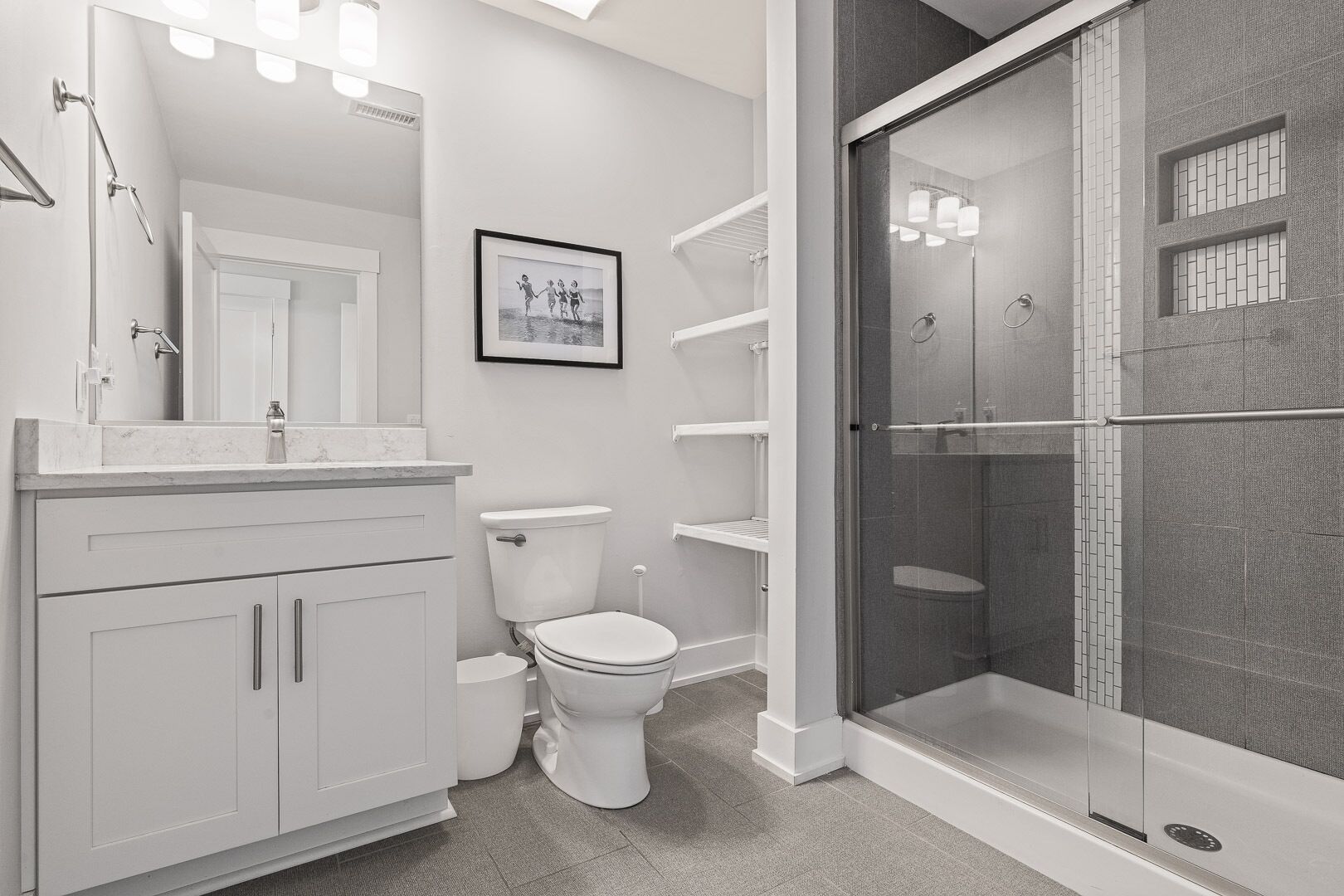 A modern bathroom with a toilet, a shower enclosure, and a vanity with a mirror and lights.