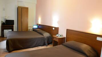 Ein Hotelzimmer mit zwei Betten, einem Holzschrank, einem Schreibtisch mit Computer und einem kleinen Tisch mit Telefon.