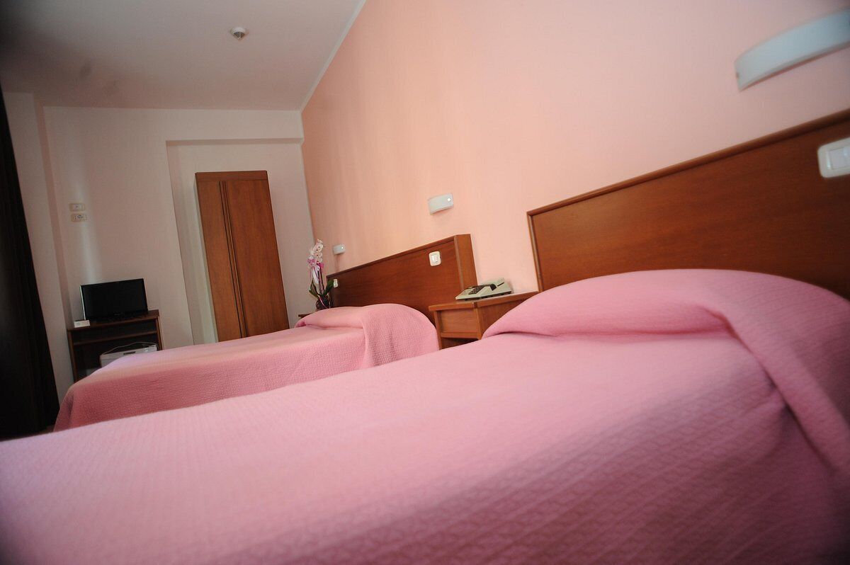 A hotel room with two beds, a wooden headboard, a nightstand, a telephone, and a door in the background.