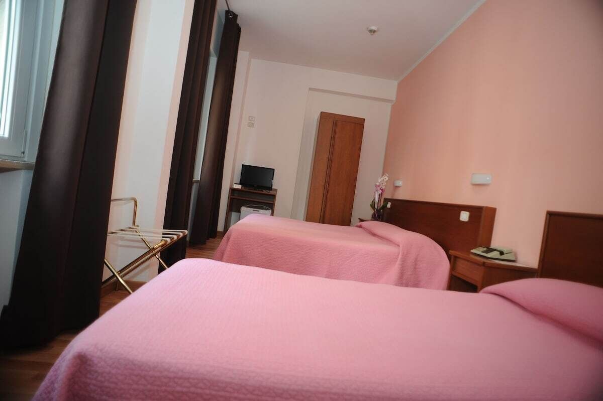 Una camera d'albergo con due letti, una televisione, un armadio e un tavolino con una lampada.