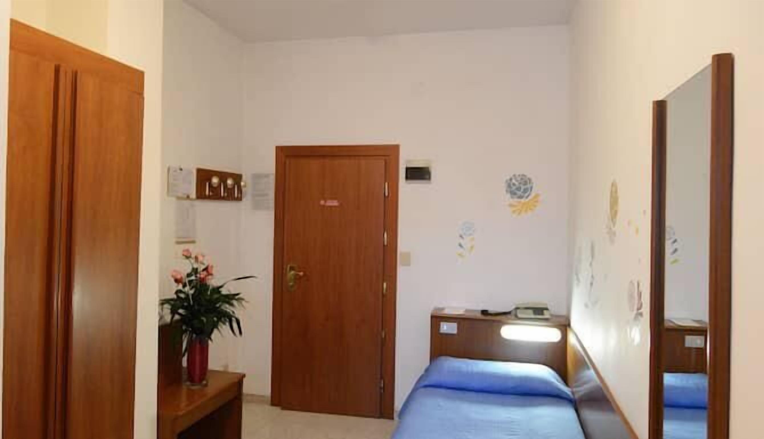 Ein Schlafzimmer mit einem Einzelbett, einem Holzschrank, einem Nachttisch mit Lampe und einem Blumentopf.