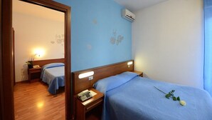 Habitación de hotel con dos camas, cabeceros de madera, mesitas de noche con lámparas, un equipo de aire acondicionado y un espejo.