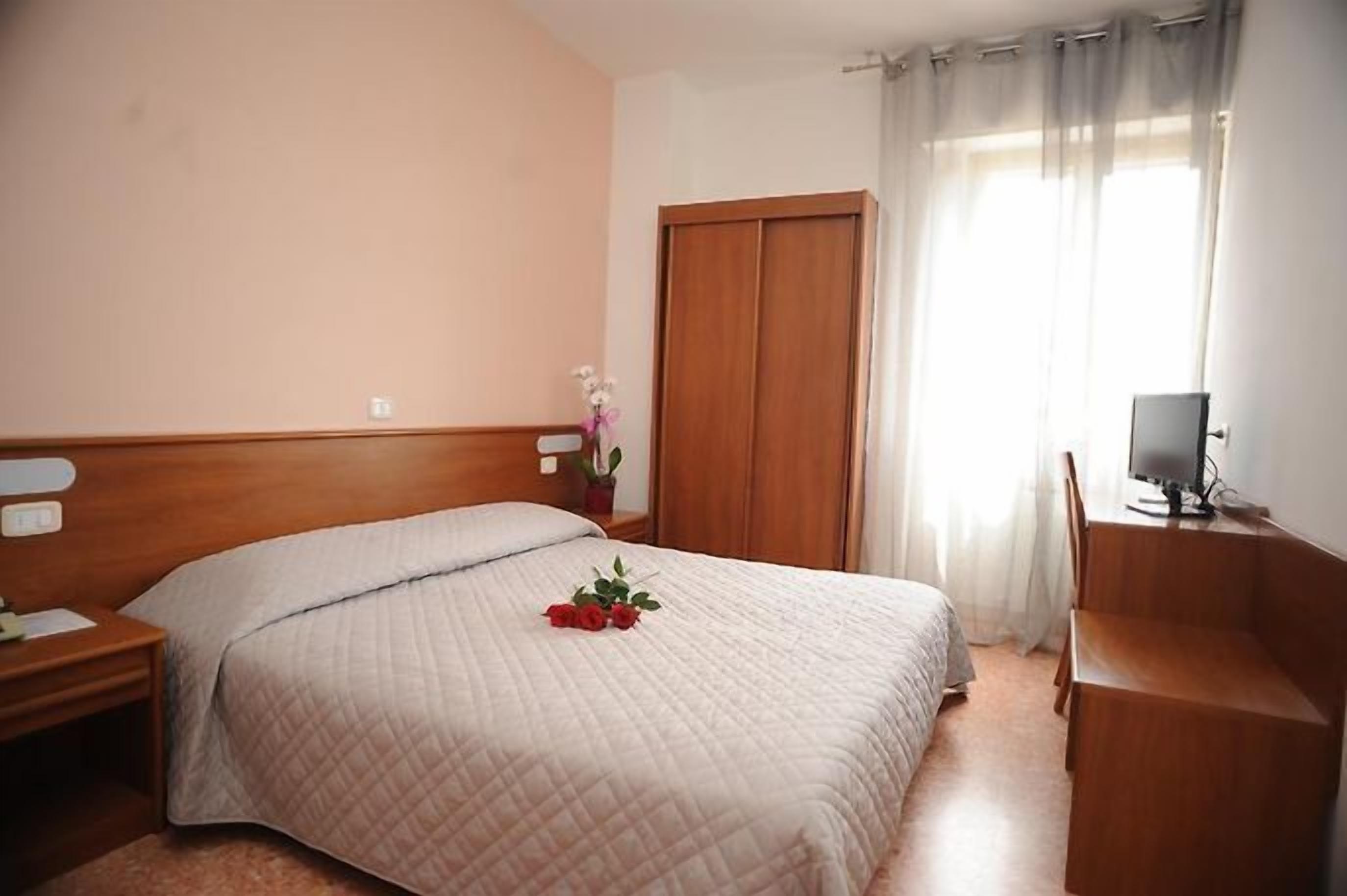 Un dormitorio con cama, escritorio, silla, armario y ventana con cortinas.