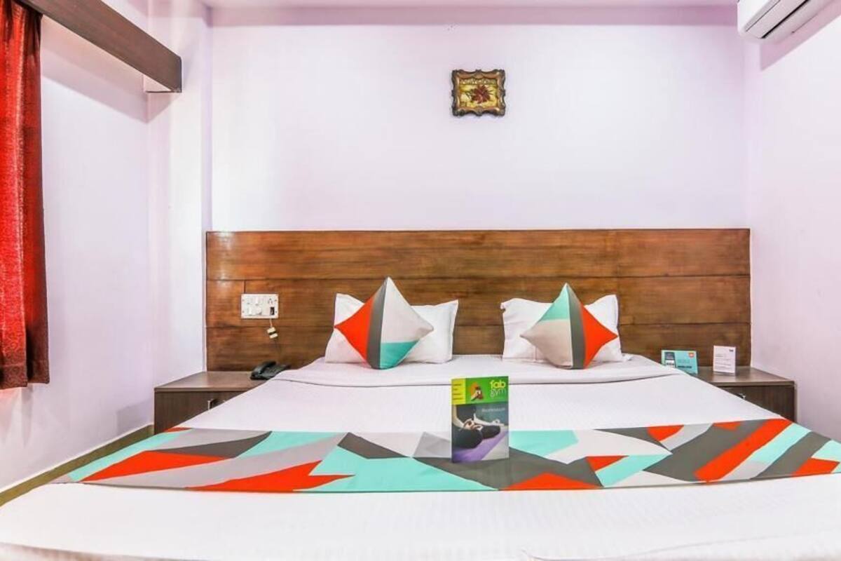 Ein Hotelzimmer mit hölzernem Kopfteil, einem Bett mit bunten Kissen, einem Nachttisch mit Telefon und einem kleinen gerahmten Bild an der Wand.