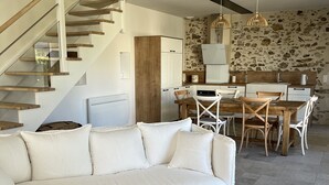 Una sala de estar moderna con un sofá blanco, una mesa de centro de madera y una zona de comedor con un fondo de pared de piedra.