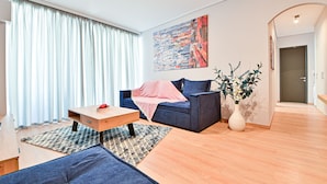 Un salón moderno con un sofá azul, una mesa de centro de madera y un amplio ventanal con cortinas blancas.