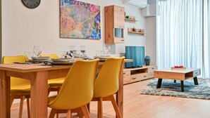 Una sala de estar moderna con comedor, un cuadro abstracto grande, un aparador de madera y un televisor.