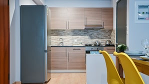 Una cocina moderna con armarios de madera, salpicadero de azulejos, horno empotrado y zona de comedor con sillas amarillas.