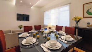 Un coin repas avec une table dressée pour six personnes, entouré de chaises rouges, d’un canapé et d’un téléviseur fixé au mur.