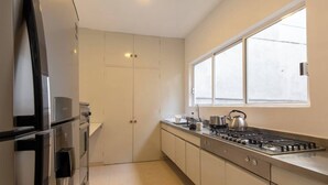 Une cuisine moderne dotée d’appareils électroménagers en acier inoxydable, d’une fenêtre avec des stores et d’un plancher de couleur claire.