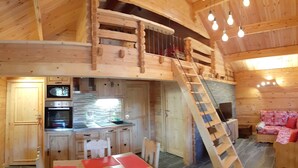 A wooden cabin interior with a kitchen, dining area, and a loft bedroom. - CHALET L'ADRET (Bluffy)