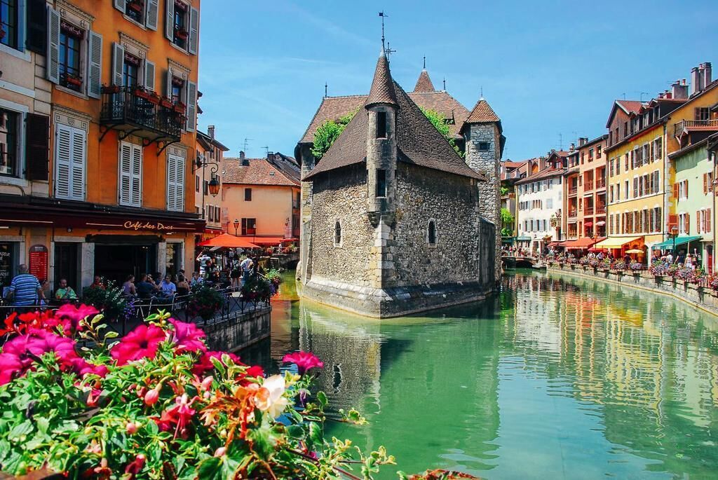 A historic stone building with a tower, surrounded by a canal with reflections.