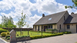 Une maison à deux étages avec un toit en pente, un petit jardin et une allée pavée.