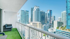 Een balkon met uitzicht op hoogbouw, een witte balustrade en een klein zitgedeelte.
