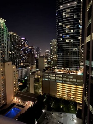 Vista noturna de um arranha-céu com janelas iluminadas e área de piscina no terraço.