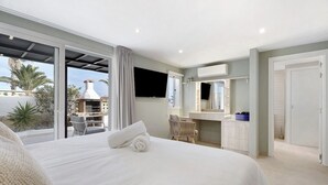 Quarto de hotel com uma cama grande, televisão, banheiro com espelho e vista para o exterior.