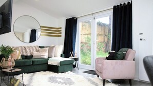 Un salon moderne avec un canapé vert, un fauteuil rose et un grand miroir au mur.