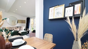 Un coin repas avec une table en bois dressée pour quatre personnes, un miroir rond et des œuvres d’art encadrées accrochées au mur.