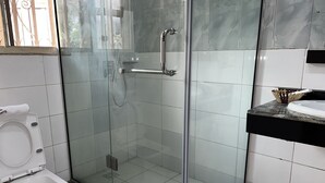 Een badkamer met een douchecabine van glas, een toilet en een wastafel met een marmeren aanrechtblad.