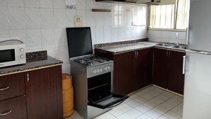Een keuken met donkere houten kastjes, een gasfornuis, een magnetron en een koelkast.