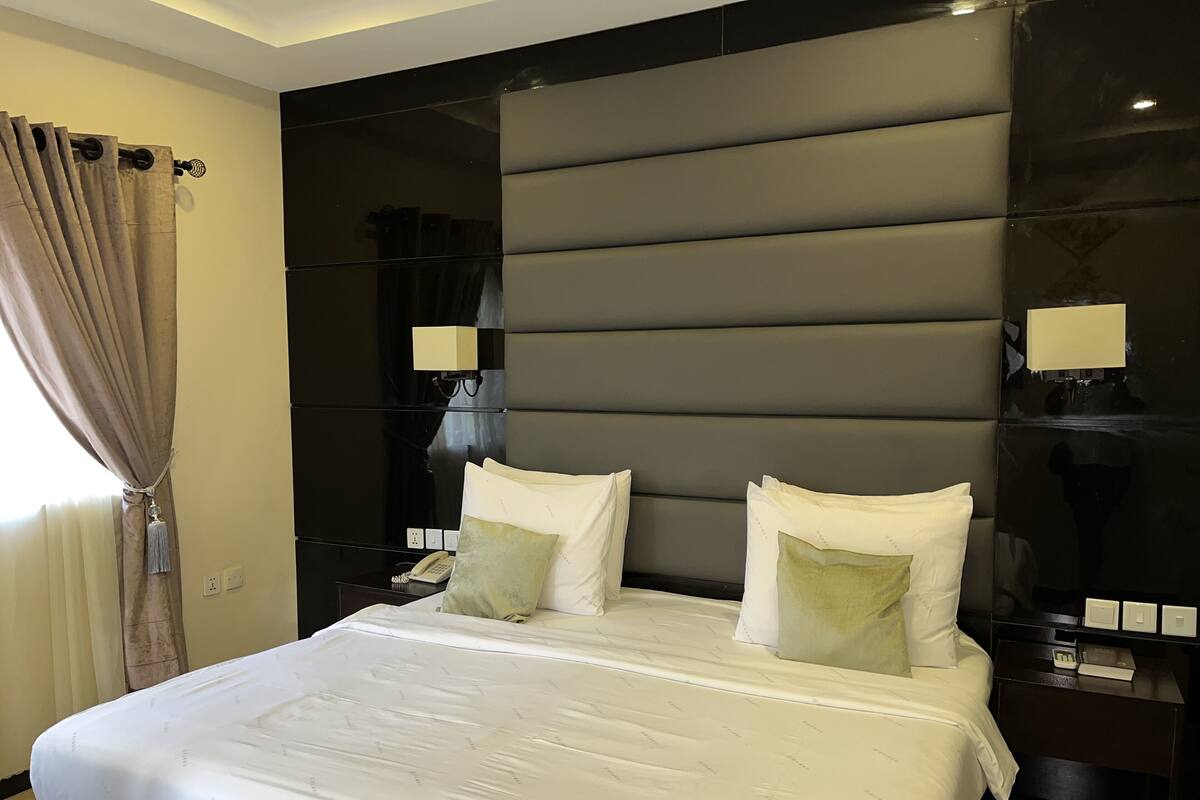 Ein modernes Hotelzimmer mit einem großen Bett, zwei Nachttischen, einer Stehlampe und einem Fenster mit Vorhängen.
