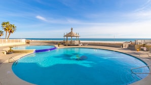 A swimming pool with a gazebo, palm trees, and a view of the ocean. - Summer House 1105A (Orange Beach)